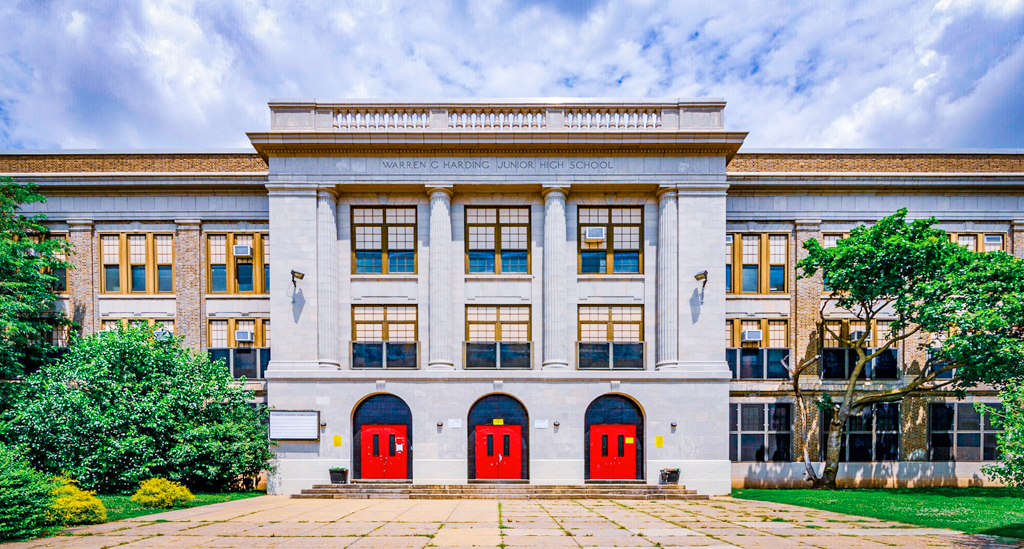 Harding Middle School Philadelphia Front Entrance Front exterior view of Harding Middle School in Philadelphia, showing the historic brick and stone building with four tall columns, large windows, and three bright red entrance doors under a partly cloudy sky.